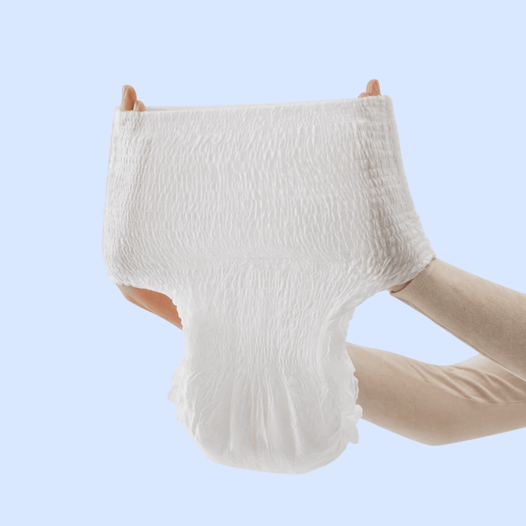 Mains étirant une culotte d'incontinence blanche absorbante pour montrer son élasticité et sa ceinture extensible confortable, sur fond bleu clair.